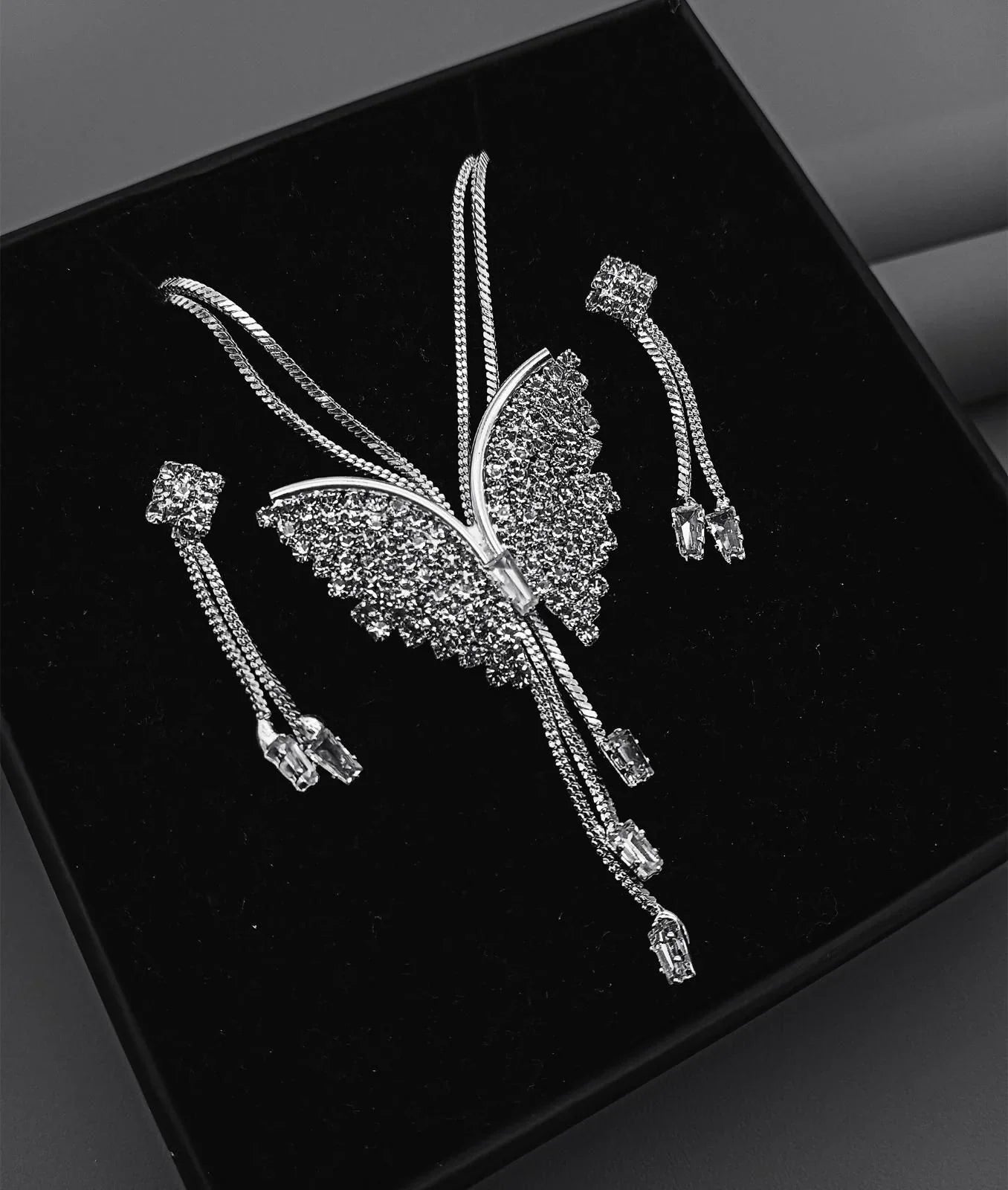 Silver butterfly brooch with rhinestones and matching dangling earrings on black velvet