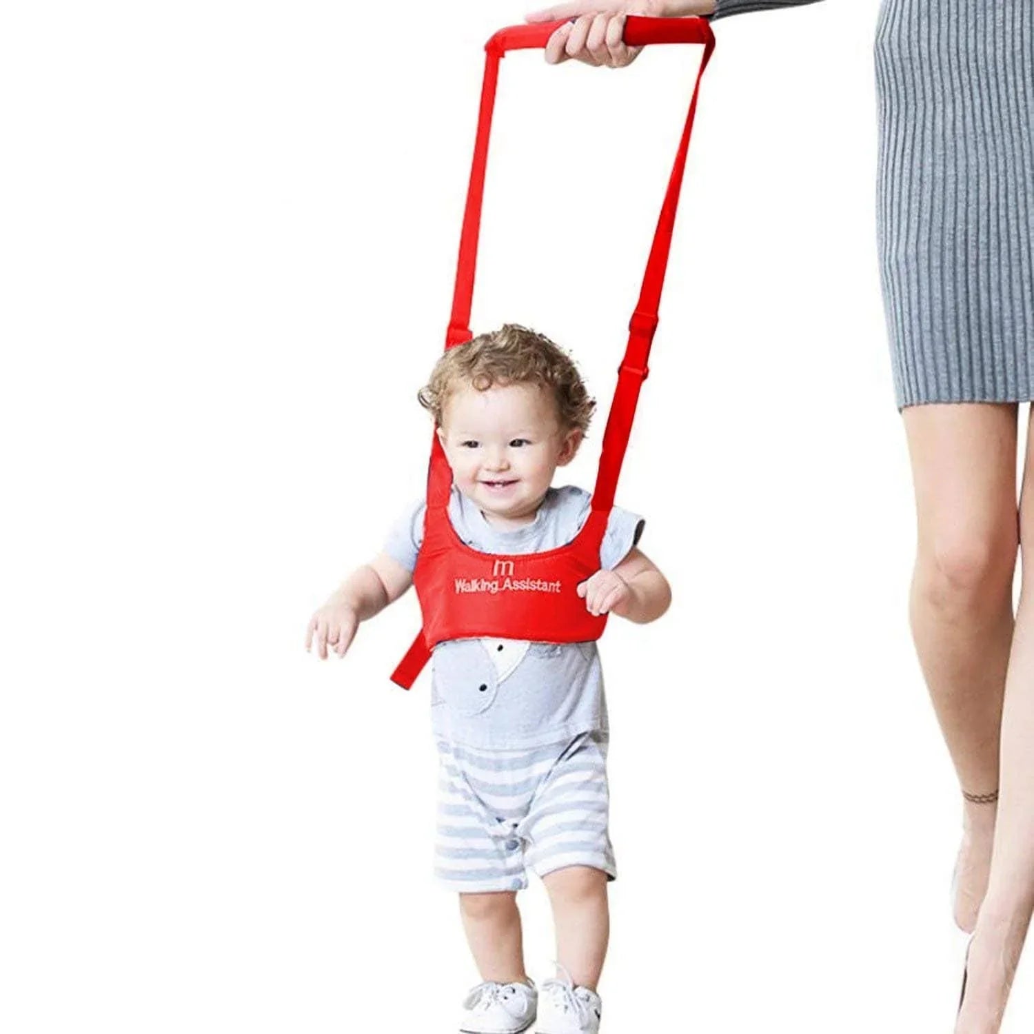 Toddler wearing a red walking assistant harness held by adult for support, learning to walk