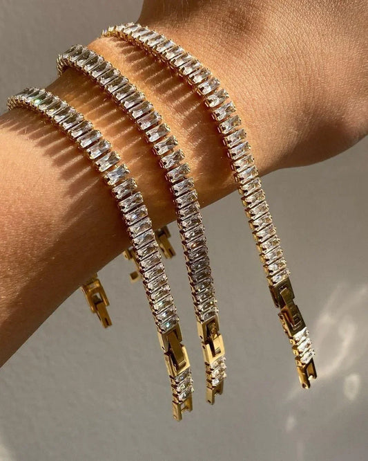 Three gold tennis bracelets with rectangular clear stones on wrist, elegant jewelry close-up