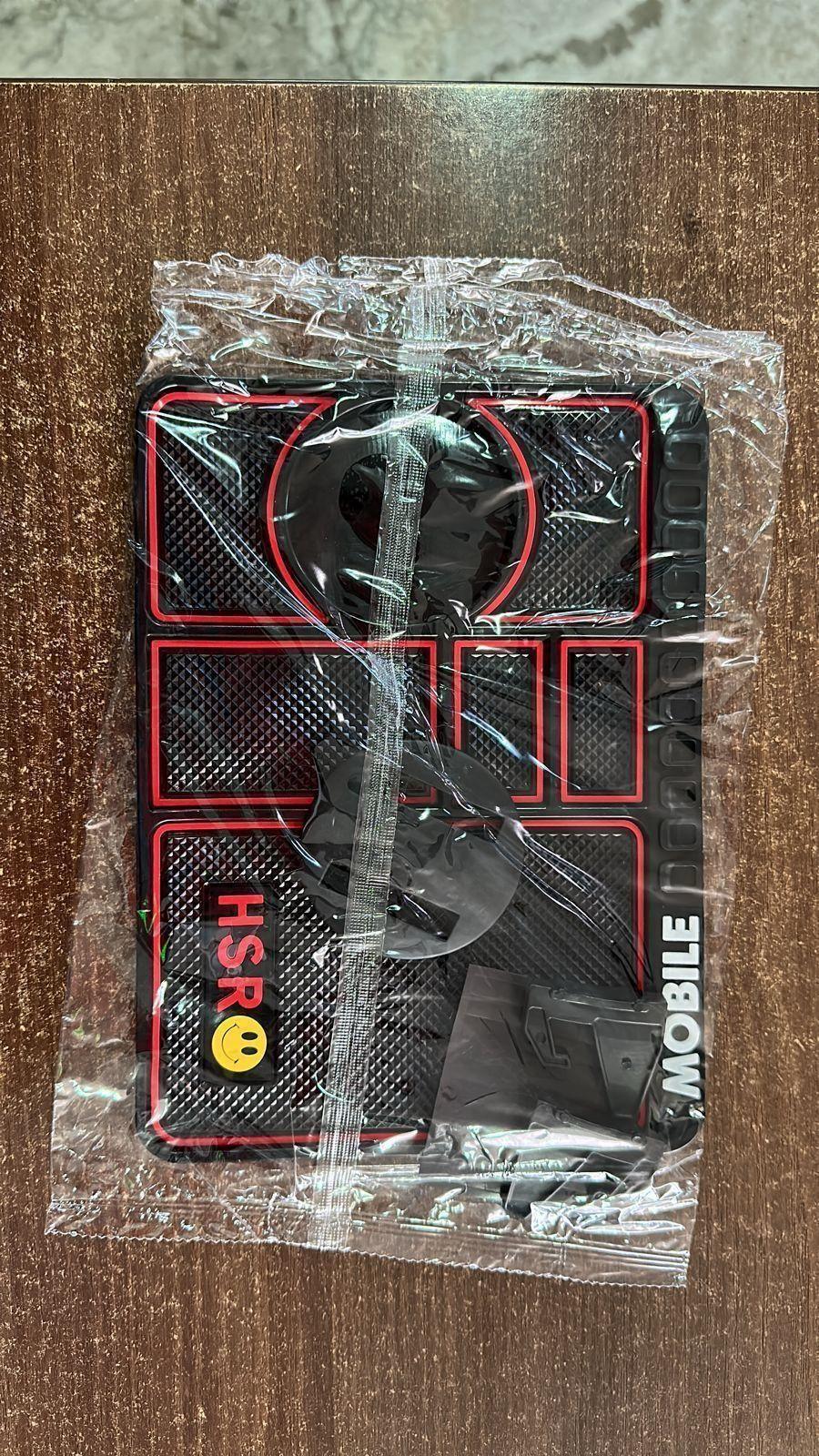 Black and red textured car dashboard anti-slip mat with suction cups in plastic packaging on wooden surface