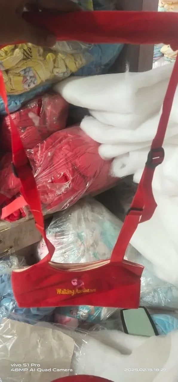 Red walking assistance belt with adjustable straps held in hand against background of packaged textile rolls and cushions