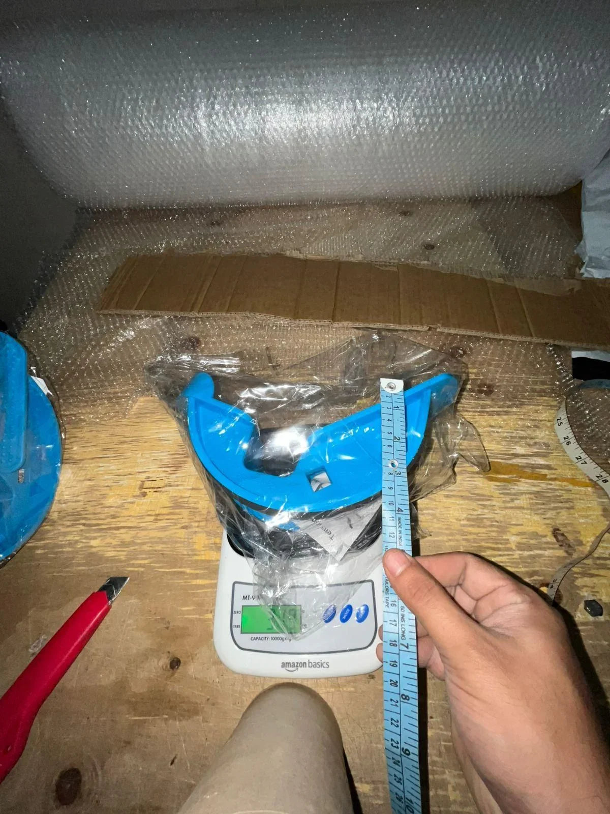 Blue plastic tool on Amazon Basics digital scale and hand holding blue measuring tape on wooden table